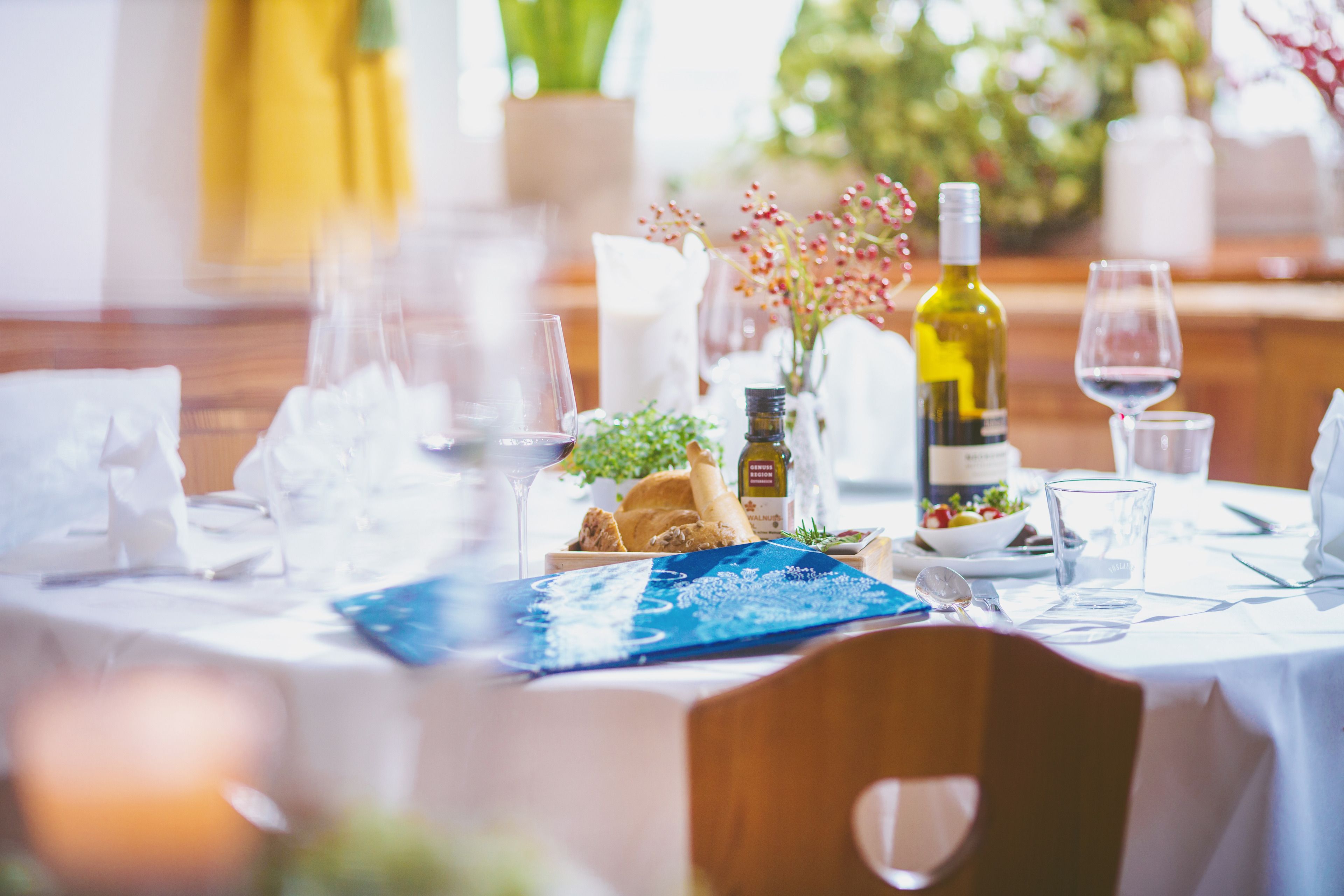 Una mesa de comedor elegantemente dispuesta con una botella de vino, copas y un tazón de ensalada.