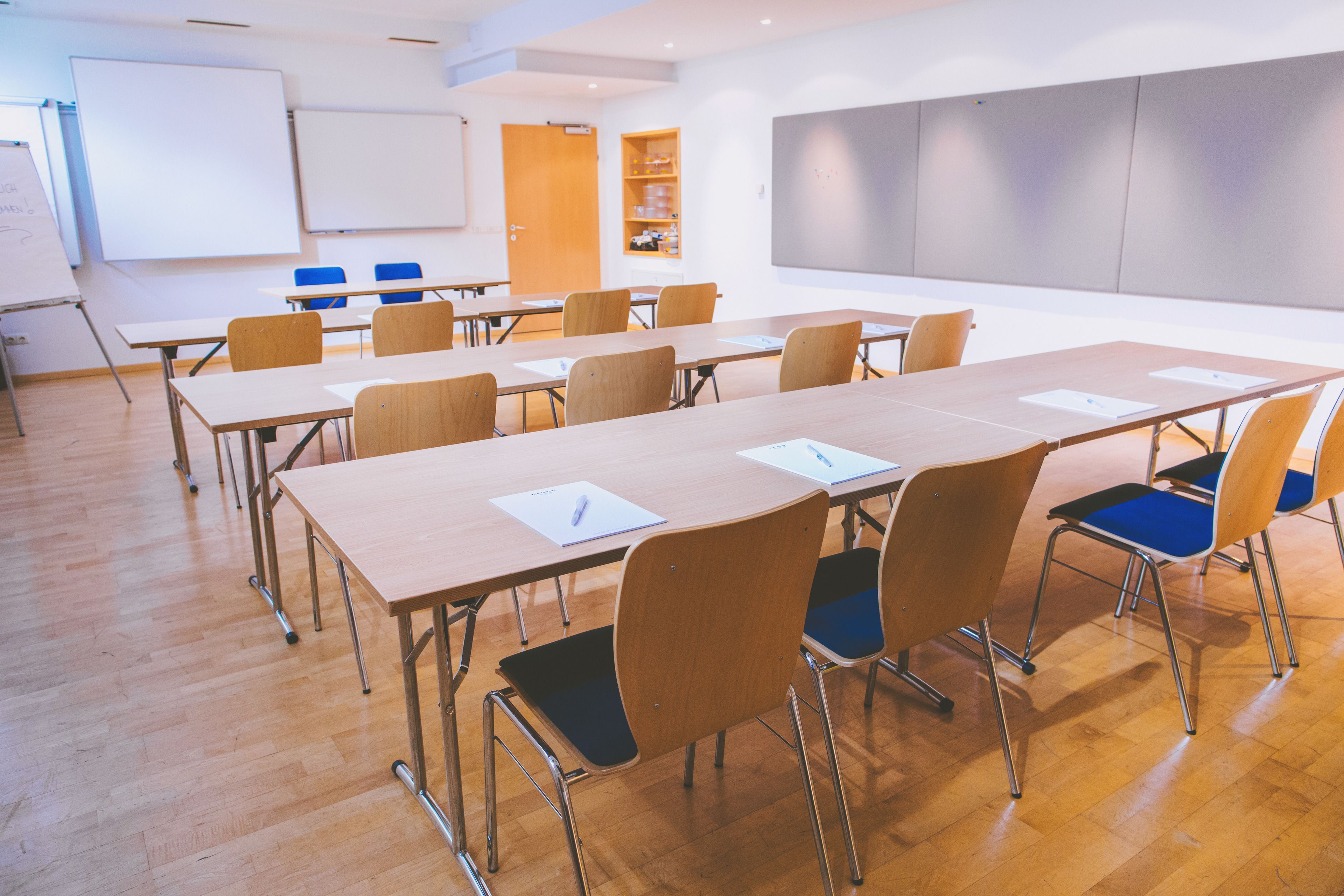 A conference room with wooden tables, chairs, a whiteboard, and a projector screen.