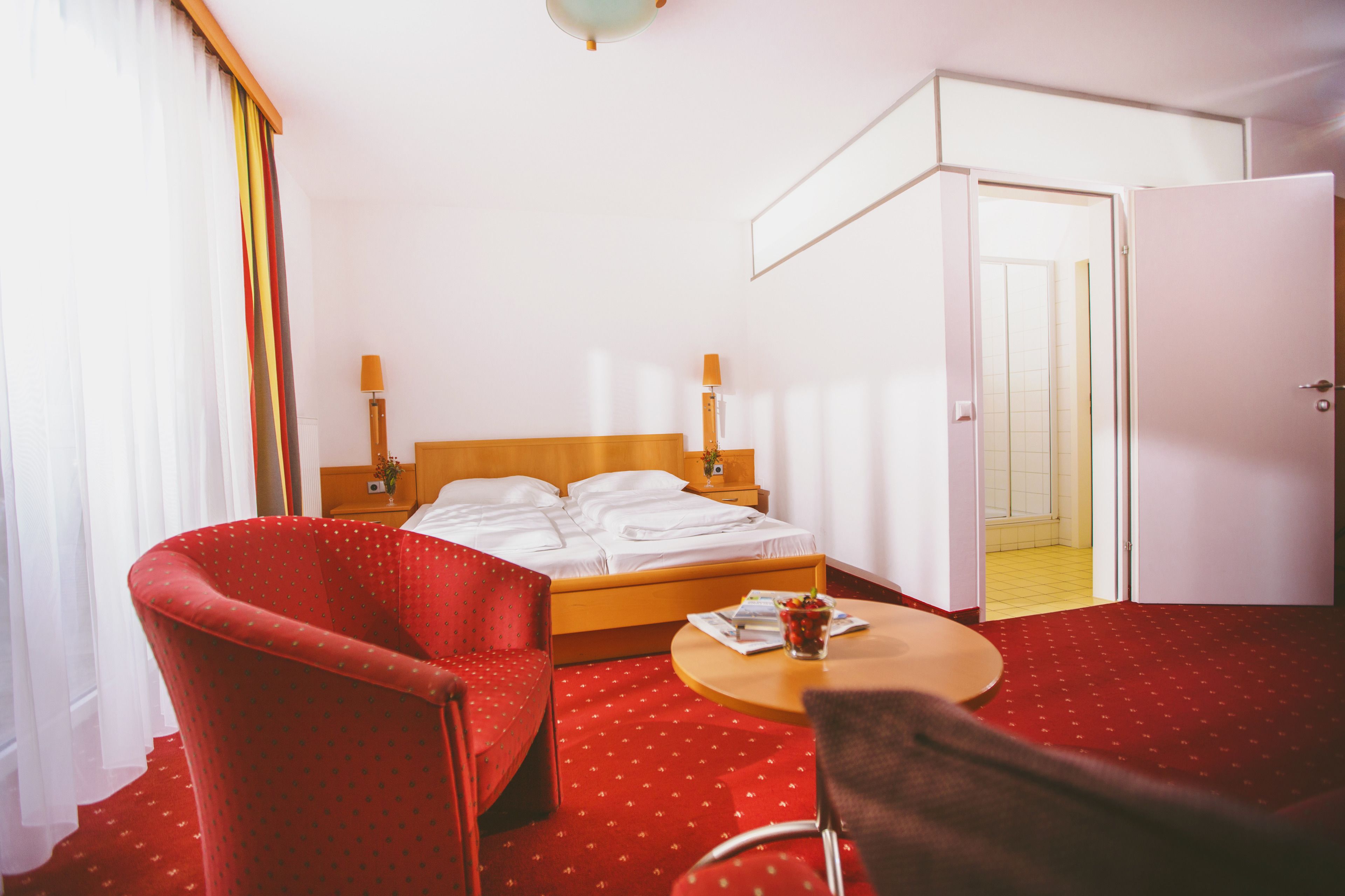 Une chambre d’hôtel comprenant un lit, deux chaises, une petite table et une porte donnant sur une salle de bain.