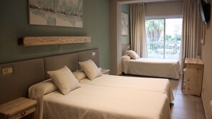 Habitación de hotel con dos camas, cabecero de madera, un cuadro en la pared, balcón con vistas y una mesita de madera.