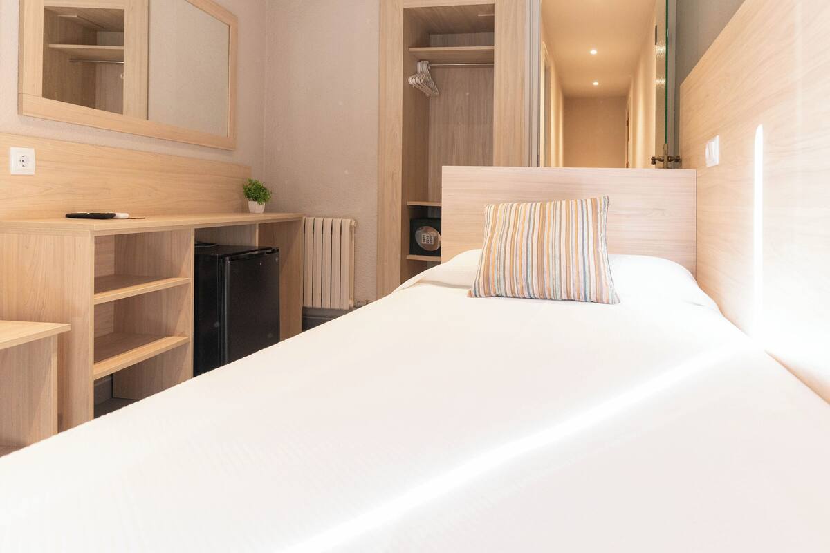 A hotel room with a bed, a bedside table, a mirror, a wardrobe, and a radiator.