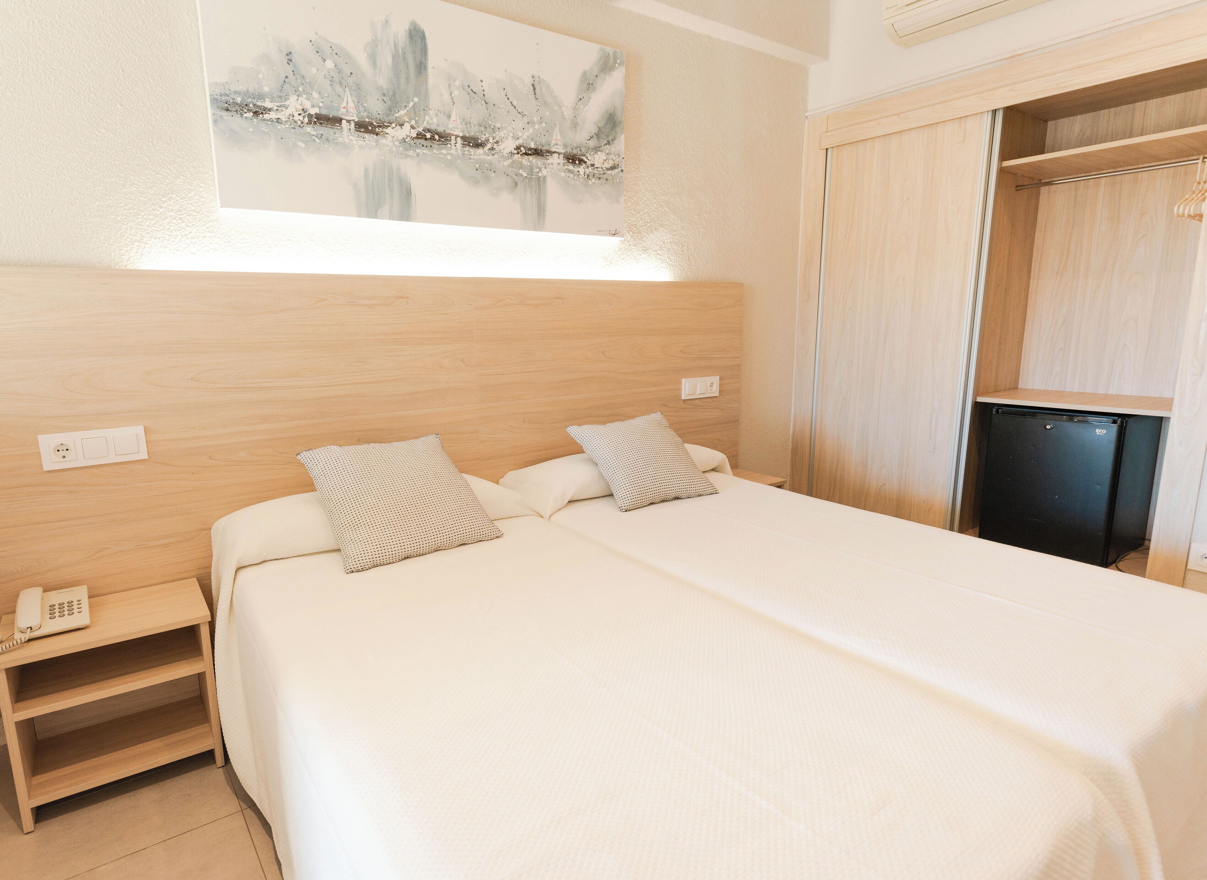 A neatly arranged bedroom with a bed, bedside tables, a small desk, and a wardrobe.