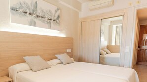 Habitación de hotel con dos camas, cabecera de madera, un cuadro en la pared y un espejo que refleja el cuarto.
