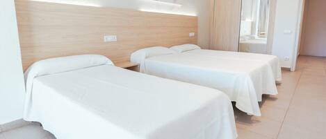 Habitación de hotel con dos camas individuales, cabecero de madera, pared blanca con un cuadro y suelo de baldosas.