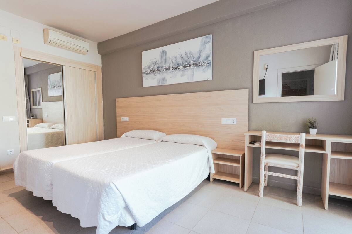A modern bedroom with a large bed, a wooden desk, and a mirror.