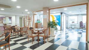 Un hall de hotel con piso de cuadros, sillas de madera, un mostrador de recepción y una planta grande en maceta.