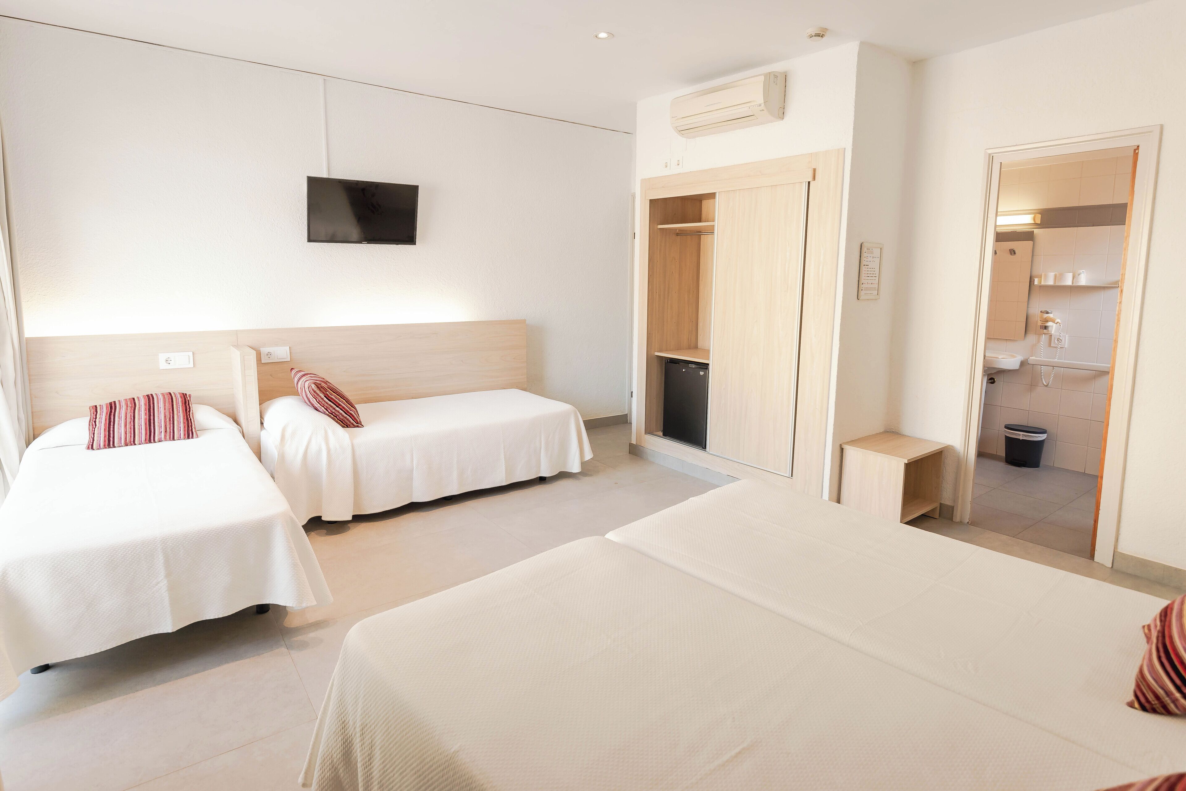 A hotel room with two single beds, a TV mounted on the wall, and a wardrobe with a mirror.