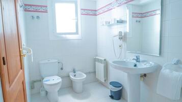 Een badkamer met toilet, bidet, wastafel en spiegel.