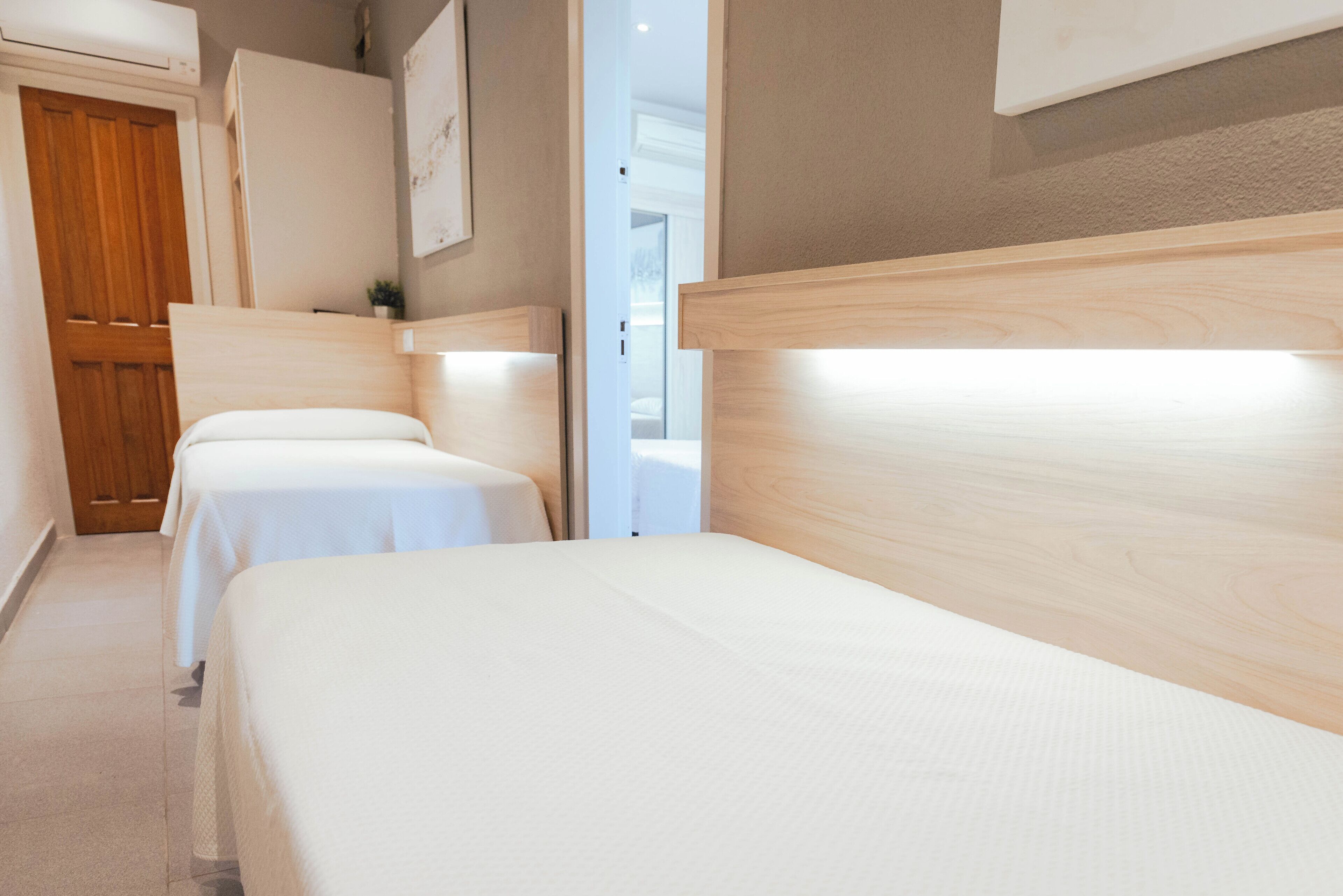 Hotelkamer met twee eenpersoonsbedden, een houten hoofdbord, een witte deur en een kleine bloempot op het nachtkastje.