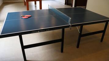 A ping pong table with two paddles in a room with a pool table in the background.