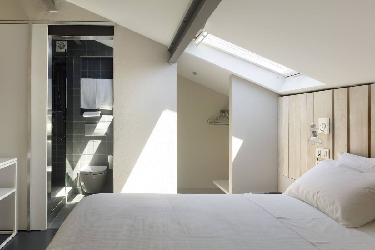 Habitación de hotel moderna con tragaluz, cama, televisor y zona de ducha.