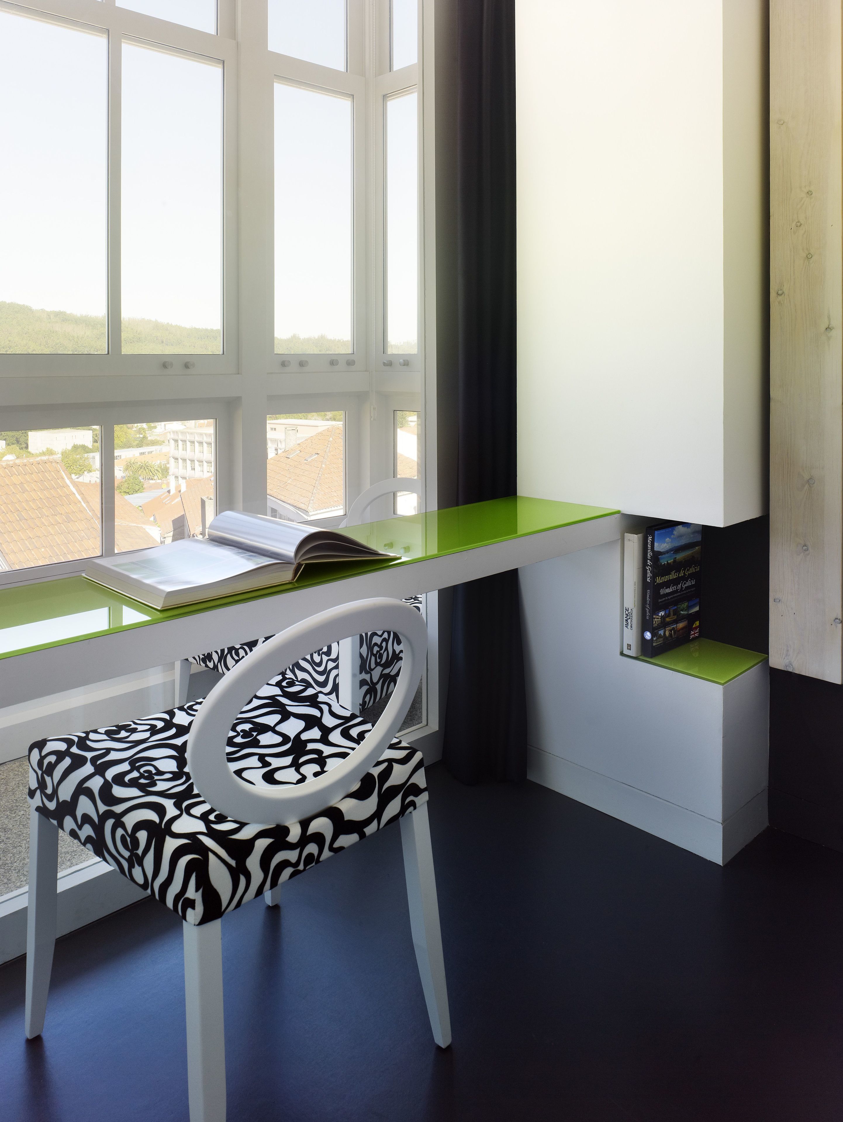 A modern office space with a white desk, a zebra-patterned chair, and a view of buildings through large windows.