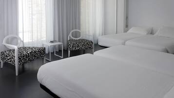 A hotel room with two single beds, a small table, two chairs, and a window with sheer curtains.