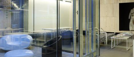 A modern interior with a glass partition, a seating area with white and patterned chairs, and a visible staircase.