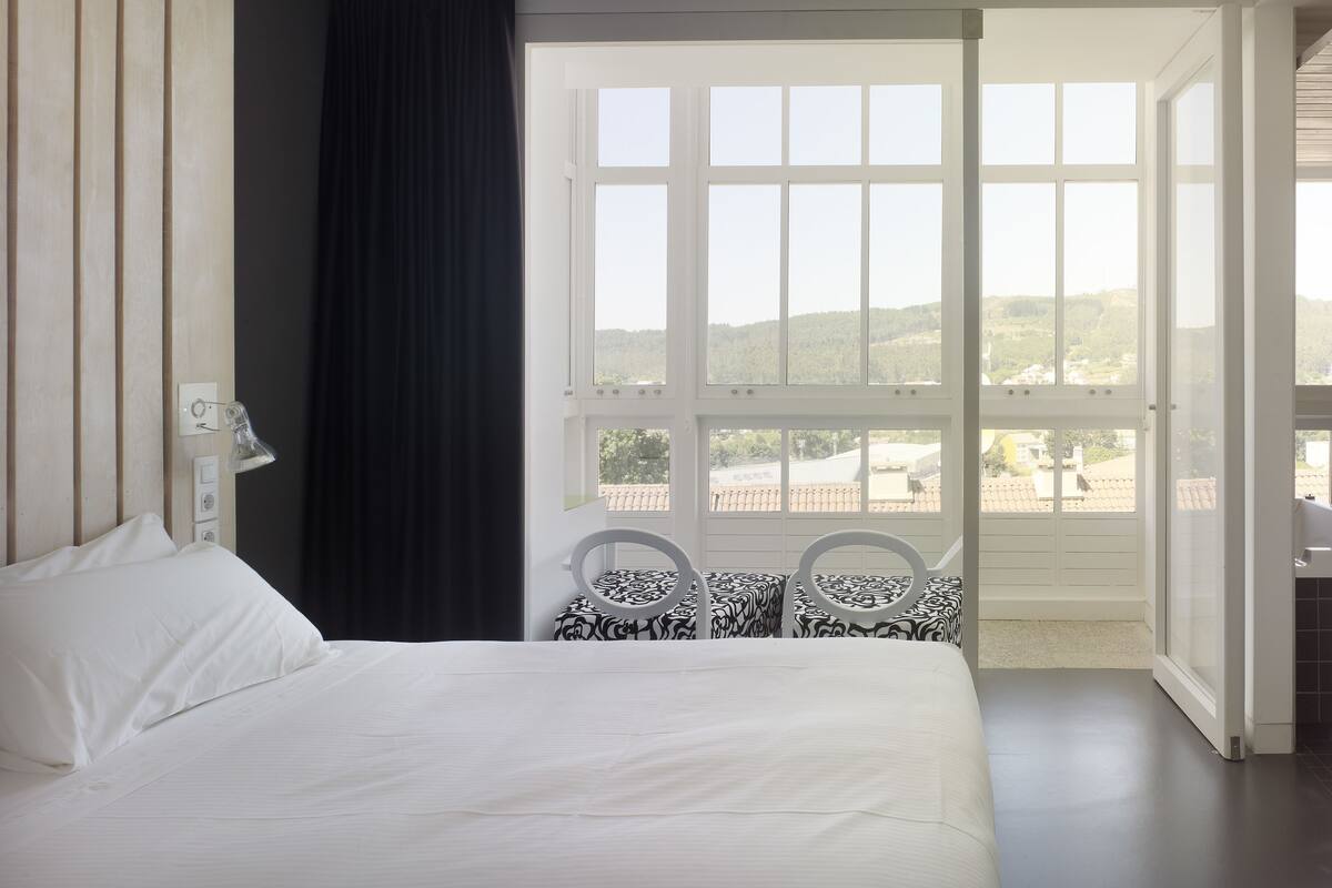 Habitación de hotel con una cama grande, ventana con vistas al campo y una pequeña mesa con sillas.