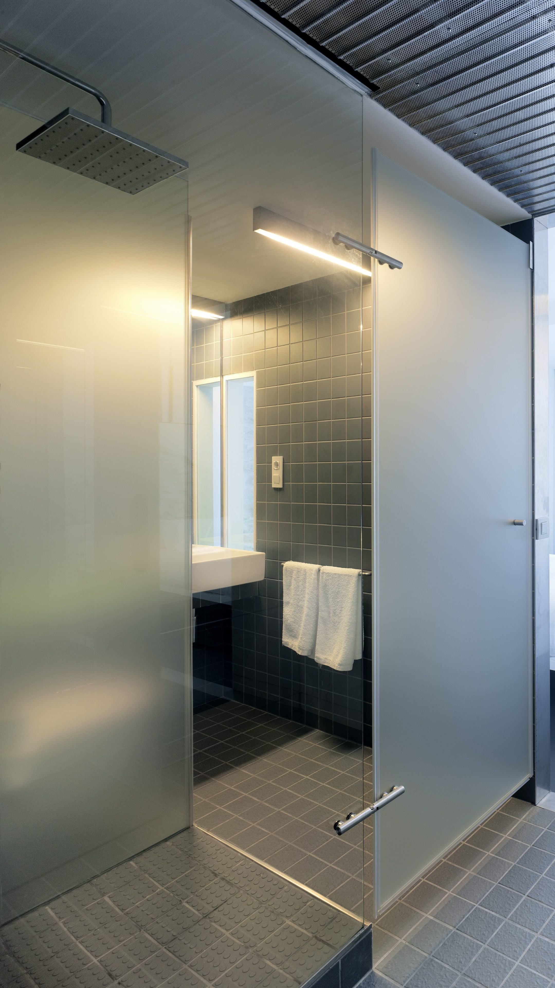 A modern bathroom with a glass partition, a white sink, a towel hanging on the wall, and a shower area.