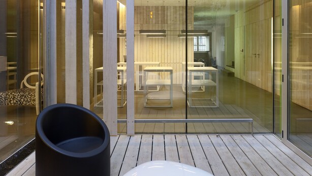 Een modern interieur met een houten vloer, glazen schuifdeuren en een zithoek met een zwart-wit stoel.