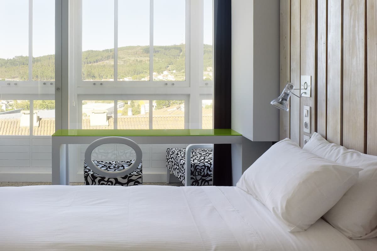 Un dormitorio con un ventanal grande, una cama, una mesita de noche y una silla.