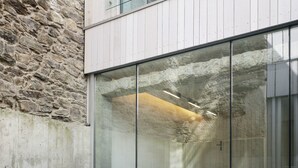 Een modern buitenmeubilairgedeelte met witte en zwarte stoelen, een tafel en een glazen wand die het interieur weerspiegelt.