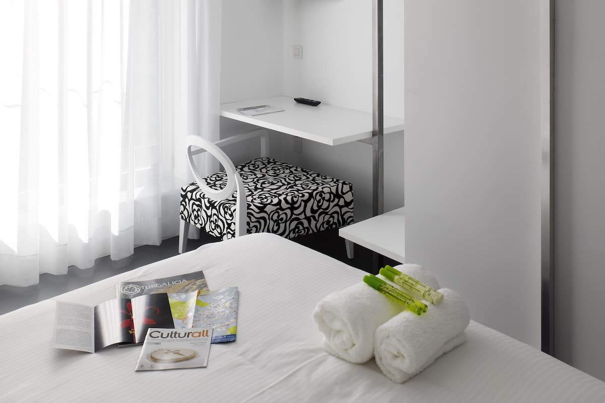 Habitación de hotel moderna con una cama bien hecha, un escritorio con televisor de pantalla plana, una silla y una mesita.