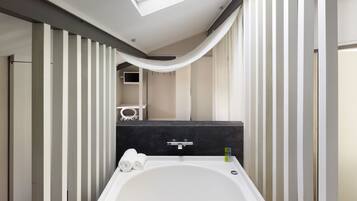 A modern bathroom with a freestanding bathtub, a vanity with a dark countertop, and a skylight above the tub.