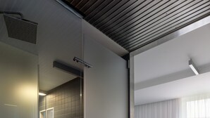Een moderne badkamer met een douchecabine van glas, een donkere betegelde muur en een wit wastafel.
