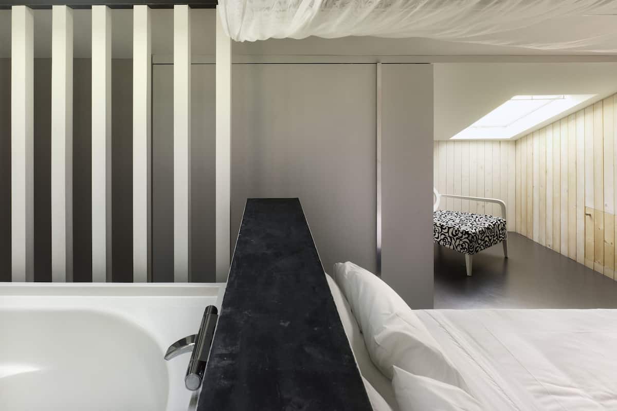 Un baño moderno con encimera negra, lavabo blanco y cama con colcha estampada.