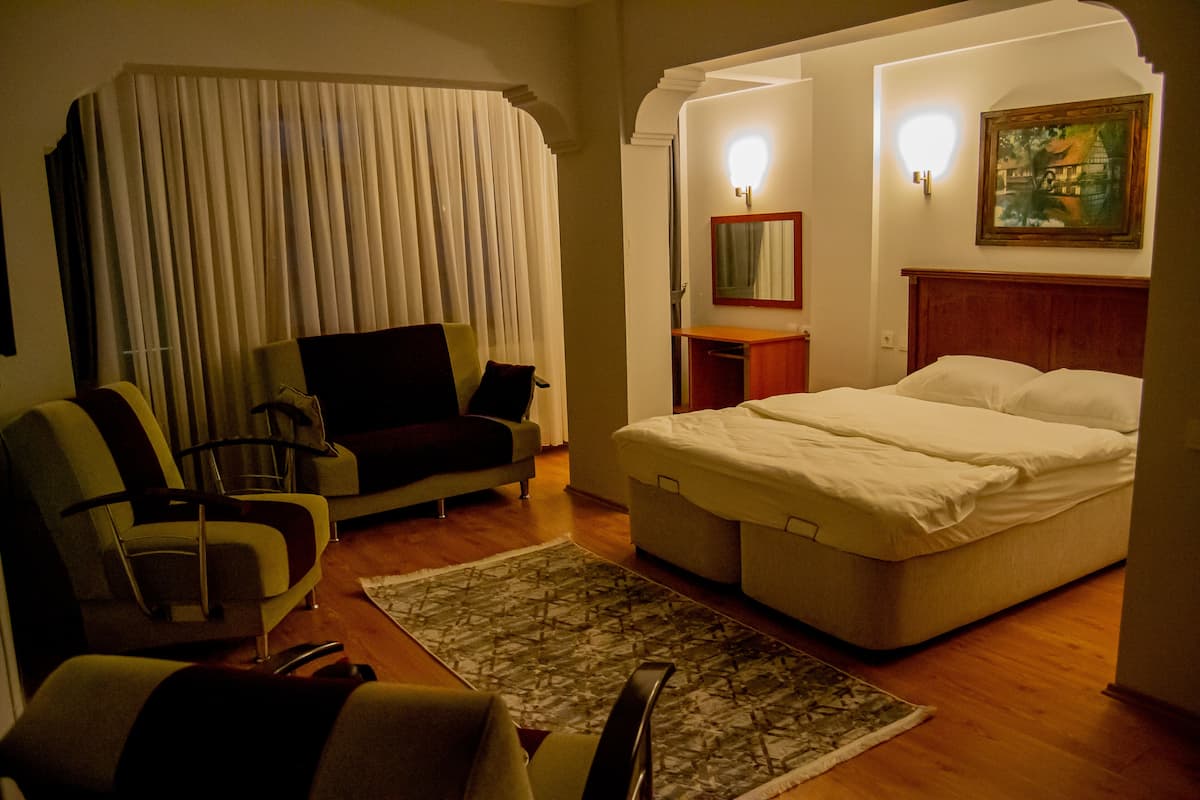 A hotel room with a bed, a sofa, a chair, a small table, and a painting on the wall.
