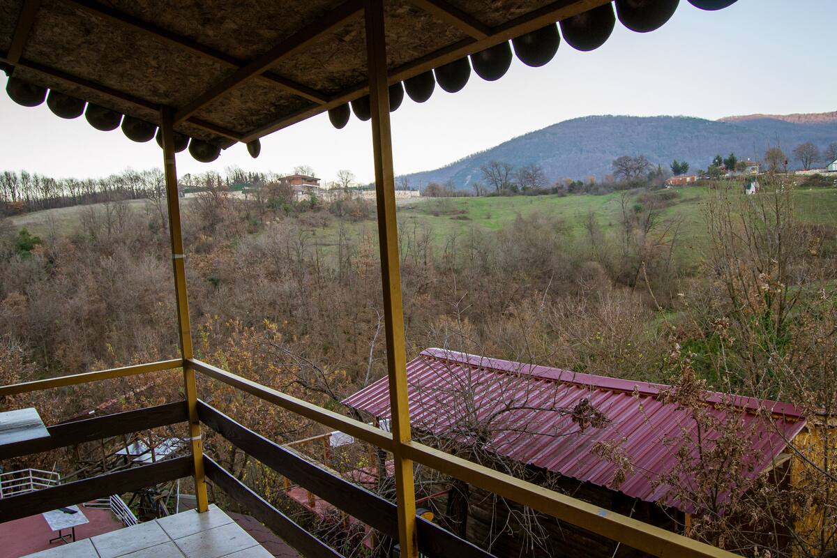 A balcony with a view of a rural landscape, including fields and distant mountains.