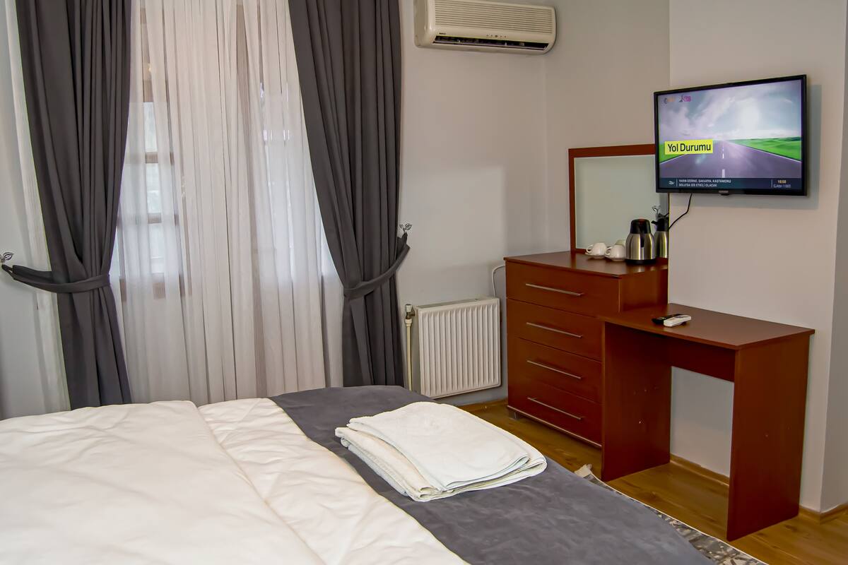 A hotel room with a bed, a desk, a TV, and a radiator.