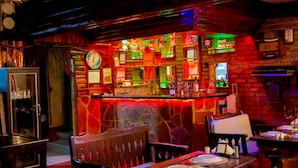 A restaurant with a rustic interior, featuring a bar area with a clock, various bottles, and a stone wall. There are wooden tables and chairs set for dining. - Kaltur Boutique Otel (Yalova)
