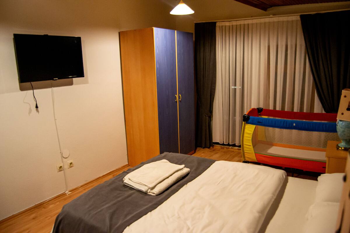 A room with a bed, a wardrobe, a television, and a window with curtains.