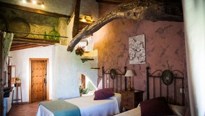 A bedroom with two beds, a wooden door, and a rustic stone wall. - Casa Rural & Spa La Graja (Chinchon)
