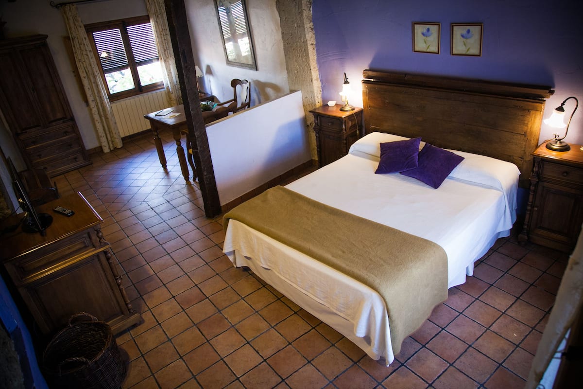 Quarto com cama grande, cabeceira de madeira, mesas de cabeceira com luminárias, cômoda e janela com cortinas.