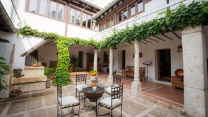 A courtyard with a round table and chairs, surrounded by potted plants and a stone floor. - Casa Rural & Spa La Graja (Chinchon)