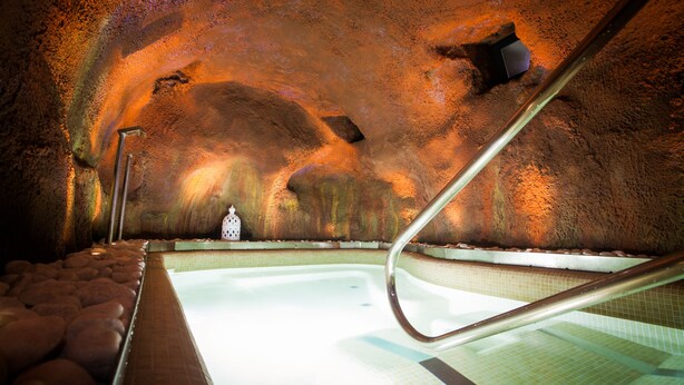 A spa with a hot tub, a tiled floor, and a rocky wall. - Casa Rural & Spa La Graja (Chinchon)