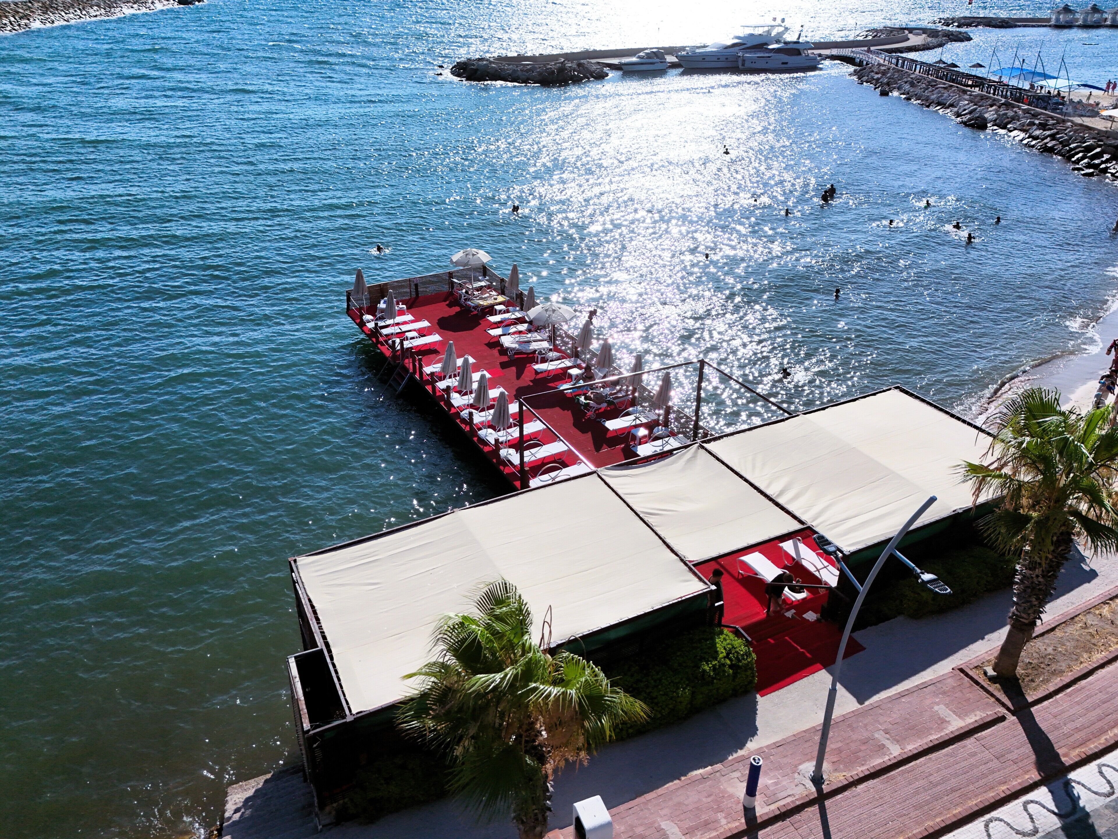 A pier with a red deck, white lounge chairs, and umbrellas, extending into a body of water.