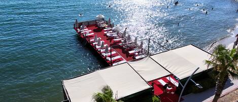 A pier with a red deck, white lounge chairs, and umbrellas, extending into a body of water.