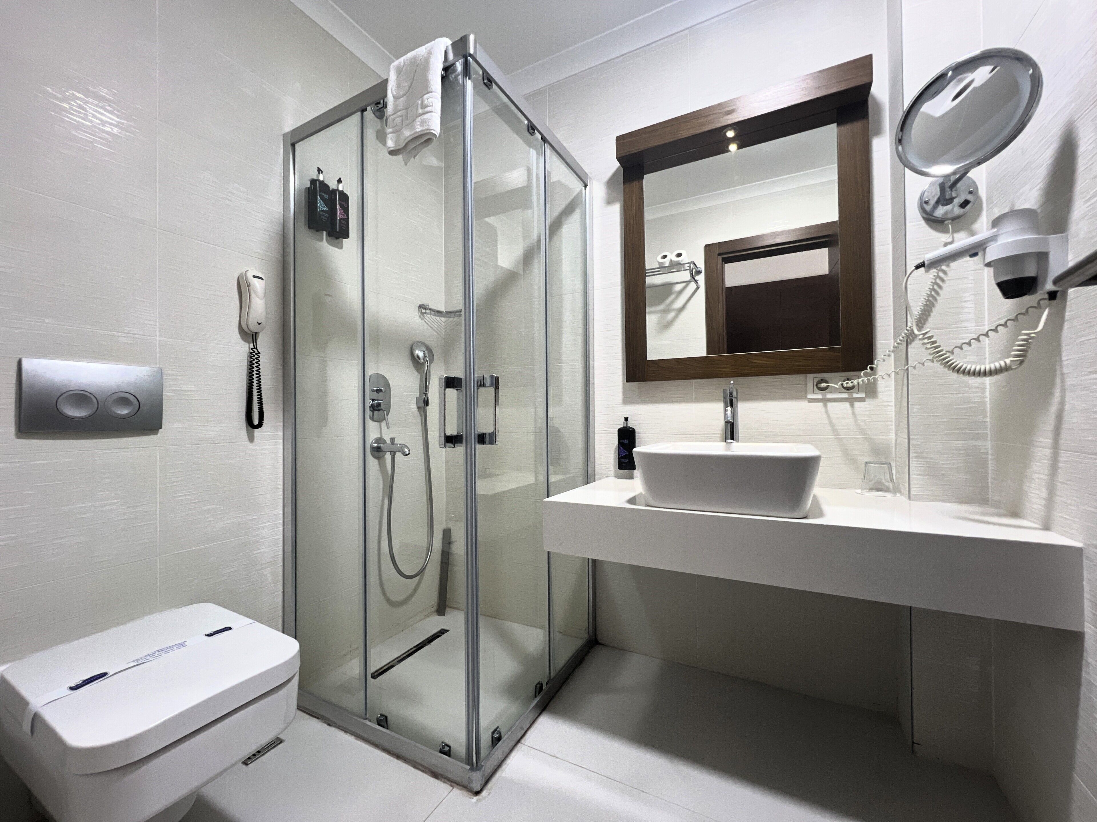 Une salle de bain moderne avec une douche à parois de verre, un lavabo blanc, un miroir et un sèche-cheveux.