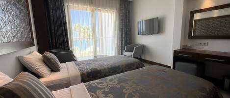 A hotel room with two beds, a desk, a chair, a TV, and a view of the outdoors.