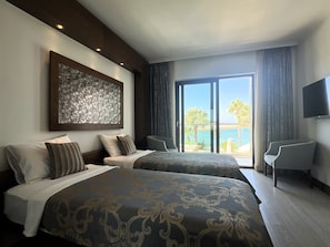 Habitación de hotel con dos camas, una obra de arte grande en la pared, un balcón con vistas y un televisor montado en la pared.