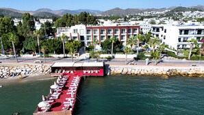 A marina with boats docked, a red-roofed building, and a backdrop of residential buildings and hills. - Veltur Turiya Hotel (Bodrum)