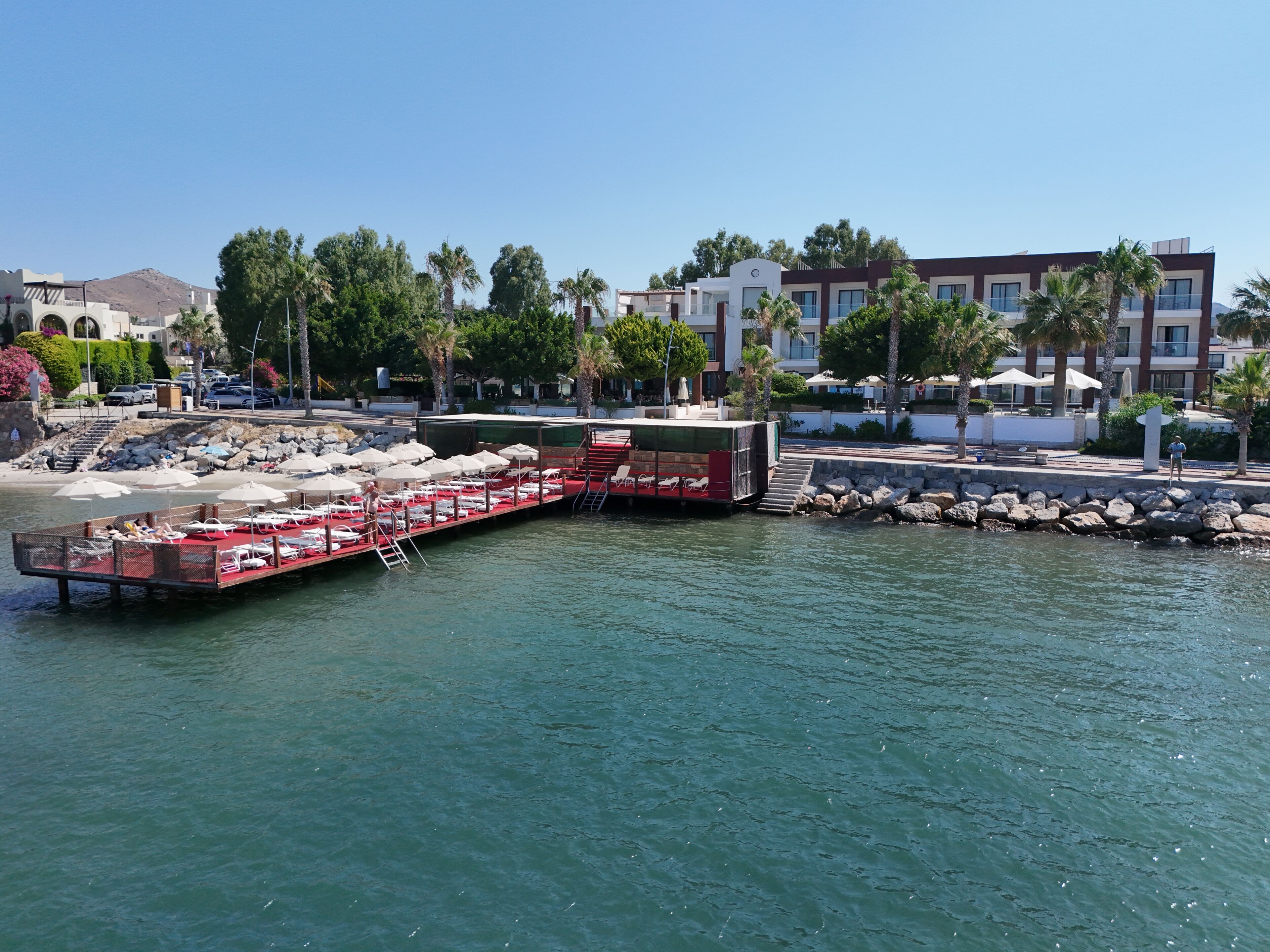 A waterfront hotel with a dock, lounge chairs, and umbrellas.