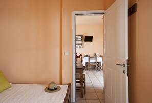A bedroom with a bed, a hat on the bed, and a door leading to a dining area with a table and chairs. - Stefano Apartments (Paros)