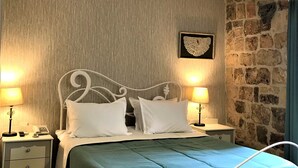 A neatly made bed with a white metal frame, two bedside tables with lamps, a stone wall, and a ceiling light fixture. - The Ninova (Antalya)