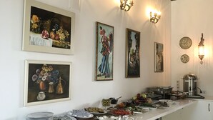 A long buffet table with various food items and plates, surrounded by wall-mounted light fixtures and framed artwork. - The Ninova (Antalya)