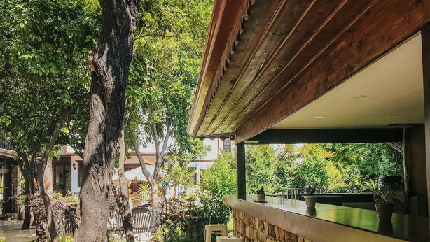 A patio area with a stone wall, a wooden pergola, and white plastic stools. - The Ninova (Antalya)
