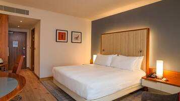 A hotel room with a large bed, a desk, a chair, and a small table.
