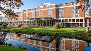 A multi-story hotel with a glass atrium, a courtyard with a pond, and a brick facade. - Hilton London Heathrow Airport Terminal 5 Hotel Conference Centre (Slough)