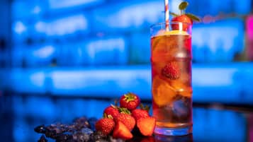 Un vaso de té helado con fresas y una hoja de menta, sobre una superficie reflectante con un fondo azul desenfocado.